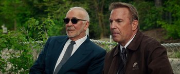 Movie still from “Draft Day” (2014), directed by Ivan Reitman – Two men in suits and ties sitting next to each other; Medium shot, Over the shoulder angle