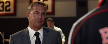 Movie still from “Draft Day” (2014), directed by Ivan Reitman – A man in a gray suit and a black tie; Close Up shot, Over the shoulder angle