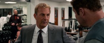 Movie still from “Draft Day” (2014), directed by Ivan Reitman – A man in a gray suit and a tie; Close Up shot, Over the shoulder angle