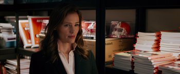 Movie still from “Draft Day” (2014), directed by Ivan Reitman – A woman in a green suit standing in front of stacks of books; Close Up shot, Over the shoulder angle