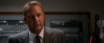 Movie still from “Draft Day” (2014), directed by Ivan Reitman – A person wearing a suit and tie; Close Up shot, Over the shoulder angle