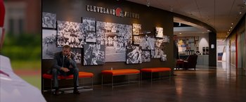 Movie still from “Draft Day” (2014), directed by Ivan Reitman – A man sitting in front of a wall of photos of cleveland browns players; Wide shot, High angle