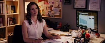 Movie still from “Draft Day” (2014), directed by Ivan Reitman – A woman sitting at a desk in front of papers; Medium shot, Over the shoulder angle