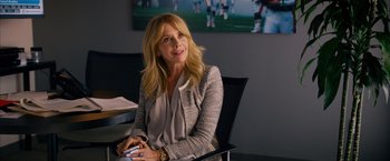 Movie still from “Draft Day” (2014), directed by Ivan Reitman – A woman sitting at a table in front of a picture; Medium shot, Over the shoulder angle