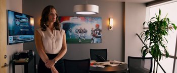 Movie still from “Draft Day” (2014), directed by Ivan Reitman – A woman standing in front of a table with papers on it; Medium shot, Over the shoulder angle