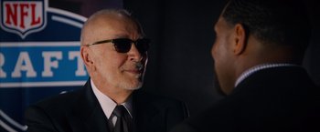 Movie still from “Draft Day” (2014), directed by Ivan Reitman – An older man wearing a suit and sunglasses talking to a younger man; Close Up shot, Over the shoulder angle
