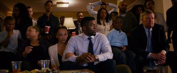 Movie still from “Draft Day” (2014), directed by Ivan Reitman – A group of people sitting in a living room watching tv; Medium shot, Over the shoulder angle