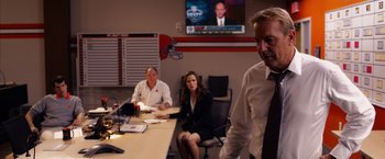Movie still from “Draft Day” (2014), directed by Ivan Reitman – A man and two women sitting in front of a television; Medium shot, Over the shoulder angle