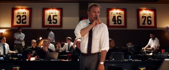 Movie still from “Draft Day” (2014), directed by Ivan Reitman – A man standing in front of a group of people; Medium shot, Over the shoulder angle