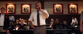 Movie still from “Draft Day” (2014), directed by Ivan Reitman – A man standing in front of a bar drinking a cup of coffee; Medium shot, Low angle