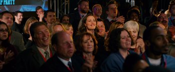Movie still from “Draft Day” (2014), directed by Ivan Reitman – A group of people sitting in a crowd clapping and smiling; Medium shot, Over the shoulder angle