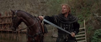 Movie still from “DragonHeart” (1996), directed by Rob Cohen – A man holding a sword near a brown horse; Medium shot, Low angle