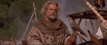Movie still from “DragonHeart” (1996), directed by Rob Cohen – A man with long hair and a beard holding a bird; Medium shot, Low angle