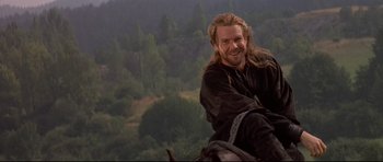 Movie still from “DragonHeart” (1996), directed by Rob Cohen – A man with long hair and a goatee is sitting on a horse; Medium shot, Over the shoulder angle