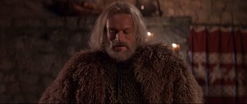 Movie still from “DragonHeart” (1996), directed by Rob Cohen – A man with long white hair and a beard wearing a fur coat; Medium shot, Low angle