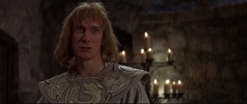 Movie still from “DragonHeart” (1996), directed by Rob Cohen – A man with long blonde hair wearing a gray and white costume; Close Up shot, Low angle