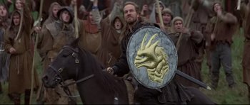 Movie still from “DragonHeart” (1996), directed by Rob Cohen – A group of men in medieval garb are gathered around a shield; Medium shot, Over the shoulder angle
