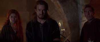 Movie still from “DragonHeart” (1996), directed by Rob Cohen – A man with long hair and beard standing in front of a stone wall; Close Up shot, Over the shoulder angle