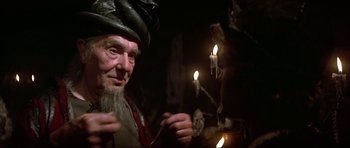 Movie still from “Dragonslayer” (1981), directed by Matthew Robbins – An old man with a beard is holding a candle; Close Up shot, Over the shoulder angle
