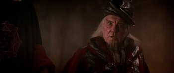 Movie still from “Dragonslayer” (1981), directed by Matthew Robbins – An old man wearing a hat and a red cape; Close Up shot, Over the shoulder angle