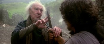 Movie still from “Dragonslayer” (1981), directed by Matthew Robbins – An older man holding a knife in his hand; Close Up shot, Over the shoulder angle