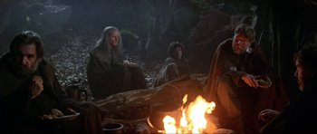 Movie still from “Dragonslayer” (1981), directed by Matthew Robbins – A group of people sitting around a campfire; Medium shot, Low angle