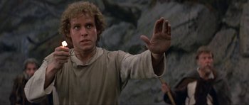 Movie still from “Dragonslayer” (1981), directed by Matthew Robbins – A man holding his hand up in the air while standing in front of a rock wall; Close Up shot, Low angle