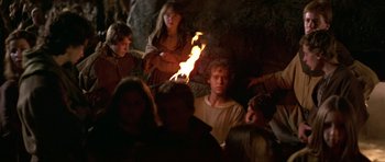 Movie still from “Dragonslayer” (1981), directed by Matthew Robbins – A group of people sitting in a cave with a fire; Medium shot, High angle