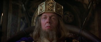 Movie still from “Dragonslayer” (1981), directed by Matthew Robbins – A man with a beard wearing a gold crown; Close Up shot, Low angle