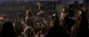 Movie still from “Dragonslayer” (1981), directed by Matthew Robbins – A crowd of people sitting and standing in front of a building; Wide shot, High angle