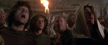 Movie still from “Dragonslayer” (1981), directed by Matthew Robbins – A group of people standing in front of a fire; Close Up shot, Over the shoulder angle