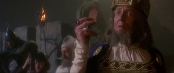 Movie still from “Dragonslayer” (1981), directed by Matthew Robbins – A man holding a piece of wood in his hand while another man looks on; Close Up shot, Over the shoulder angle