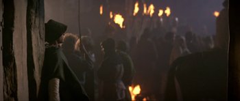 Movie still from “Dragonslayer” (1981), directed by Matthew Robbins – A group of people standing next to a fire; Medium shot, Over the shoulder angle