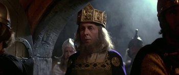 Movie still from “Dragonslayer” (1981), directed by Matthew Robbins – A man wearing a gold crown and a black robe; Close Up shot, Low angle