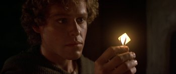 Movie still from “Dragonslayer” (1981), directed by Matthew Robbins – A young man holding a lit candle in a dark room; Close Up shot, High angle