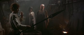 Movie still from “Dragonslayer” (1981), directed by Matthew Robbins – A man and a woman standing next to each other; Medium shot, Over the shoulder angle