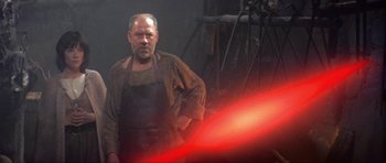 Movie still from “Dragonslayer” (1981), directed by Matthew Robbins – A man in an apron standing in front of a light saber; Medium shot, Low angle