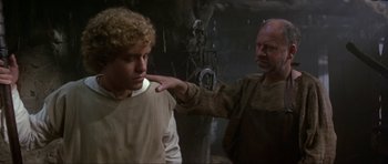Movie still from “Dragonslayer” (1981), directed by Matthew Robbins – An older man touching a younger man's shoulder; Medium shot, Over the shoulder angle