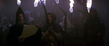 Movie still from “Dragonslayer” (1981), directed by Matthew Robbins – A man in a hooded cloak holding a staff; Medium shot, Over the shoulder angle