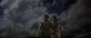 Movie still from “Dragonslayer” (1981), directed by Matthew Robbins – A man and a woman dressed in medieval garb standing next to each other in front of a cloudy sky; Wide shot, Low angle