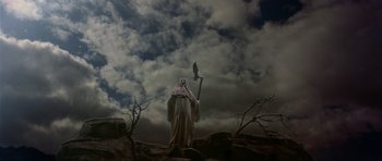 Movie still from “Dragonslayer” (1981), directed by Matthew Robbins – An old man with a long white beard holding a staff in front of a cloudy sky; Wide shot, Low angle