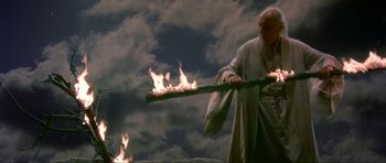 Movie still from “Dragonslayer” (1981), directed by Matthew Robbins – A man is holding a stick with flames coming out of it; Medium shot, Low angle