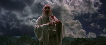Movie still from “Dragonslayer” (1981), directed by Matthew Robbins – An image of an old man holding a cross; Medium shot, Low angle