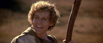Movie still from “Dragonslayer” (1981), directed by Matthew Robbins – A man smiling while holding a stick in his hand; Close Up shot, Over the shoulder angle