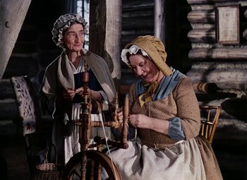 Movie still from “Drums Along the Mohawk” (1939), directed by John Ford – Two women in old - fashioned clothing working a spinning wheel; Medium shot, High angle