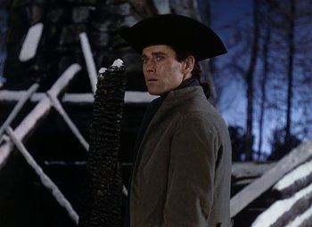 Movie still from “Drums Along the Mohawk” (1939), directed by John Ford – A man wearing a hat and holding a stick; Medium shot, Low angle