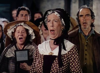 Movie still from “Drums Along the Mohawk” (1939), directed by John Ford – An older woman singing in front of a group of older people; Medium shot, Low angle