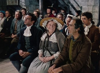 Movie still from “Drums Along the Mohawk” (1939), directed by John Ford – A group of men and women sitting next to each other; Medium shot, High angle