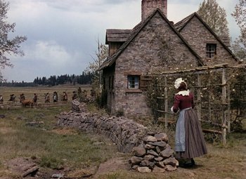 Movie still from “Drums Along the Mohawk” (1939), directed by John Ford – An old woman in an old fashioned dress standing in front of an old stone house; Extreme Wide shot, Over the shoulder angle