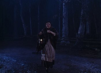 Movie still from “Drums Along the Mohawk” (1939), directed by John Ford – A woman holding a lantern while standing in a dark forest; Wide shot, Low angle